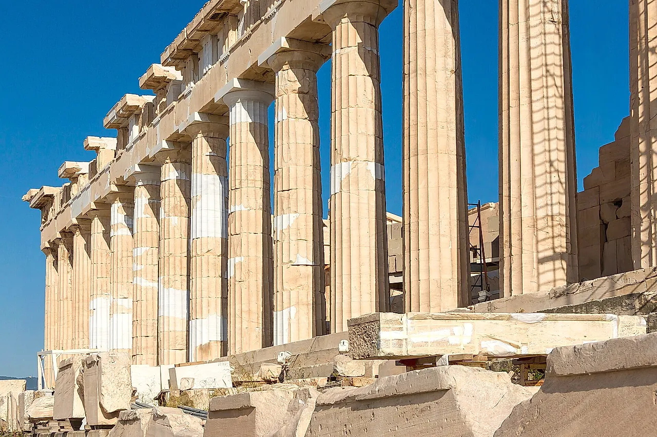 The Doric colonnade of the Parthenon seen along its side, marble columns lined up under a blue sky
