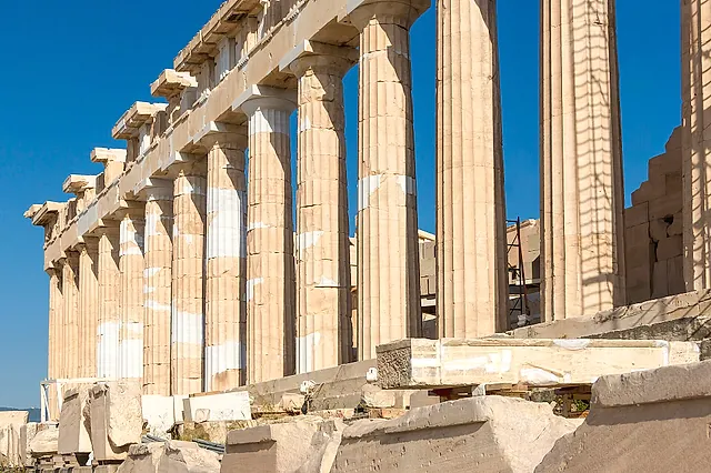The Doric colonnade of the Parthenon seen along its side, marble columns lined up under a blue sky