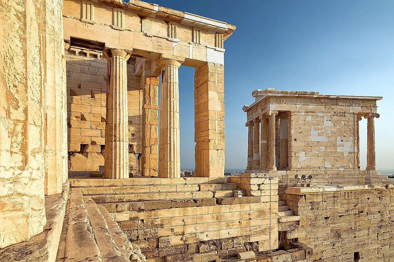 The Propylaea of the Acropolis with the small Temple of Athena Nike on its bastion, in golden stone against a blue sky
