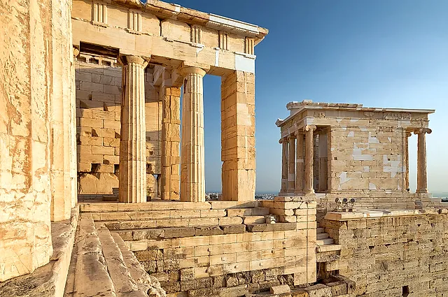 The Propylaea of the Acropolis with the small Temple of Athena Nike on its bastion, in golden stone against a blue sky