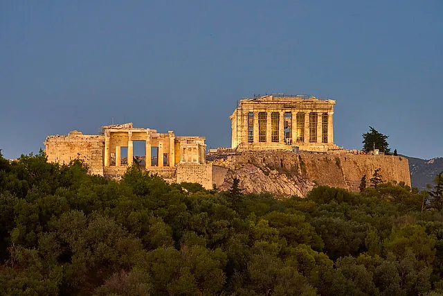 The Propylaea and the Parthenon crowning the Acropolis rock in warm evening light above the green trees